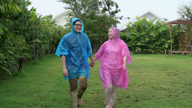 幸福的情侣穿着粉色和蓝色的雨衣，在雨中玩耍，在后院打转。视频素材