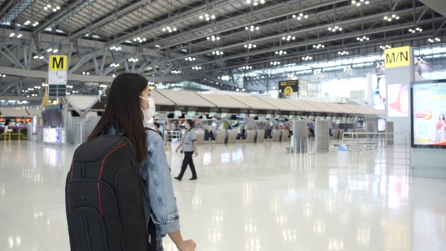 穿着蓝色牛仔裤的亚洲女乘客拖着带轮子的行李箱进入客运大楼视频素材