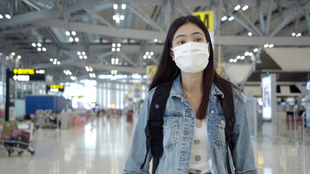 穿着蓝色牛仔裤的亚洲女乘客拖着带轮子的行李箱进入客运大楼视频素材