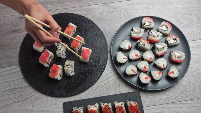 女人用筷子拿食物。日本食品成分。各种寿司摆放在黑石板上。辣泡菜沙拉，馄饨汤，筷子和酱油碗视频素材