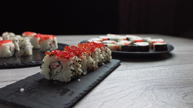 女人用筷子拿食物。寿司卷日本食物旋转在黑色的背景。加州寿司卷配金枪鱼，蔬菜，飞鱼卵和鱼子酱近距离旋转。日本餐厅菜单。4 k生视频素材