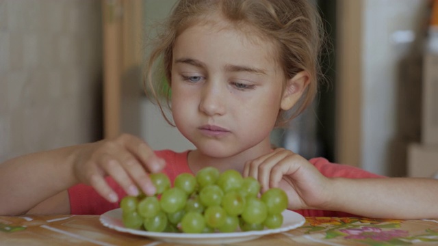 孩子吃甜葡萄。素食小女孩坐在厨房的餐桌上吃盘子里的白葡萄。健康有机素食。水果的收成。视频素材