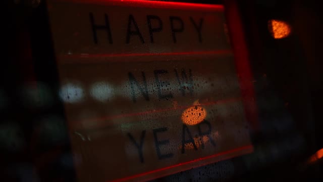 夜雨时分，在咖啡馆的玻璃门后面挂着“新年快乐”的彩色霓虹灯视频素材