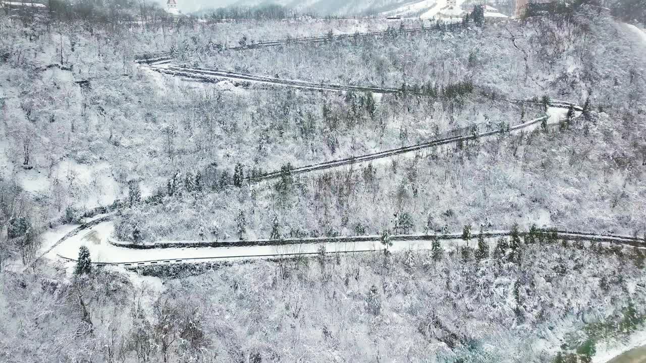 鸟瞰图弯曲的山路上山穿过松树和其他树木覆盖在冬天的雪。山在四川西岭。视频素材