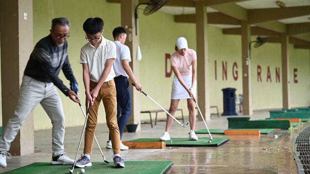 下雨的时候，一个亚洲华人小男孩和他的父母在练习场练习高尔夫视频素材