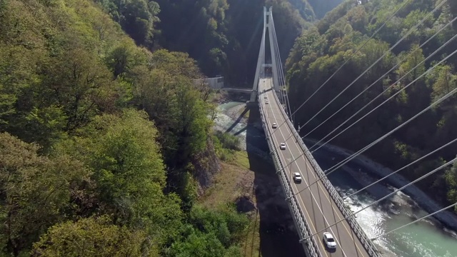 飞行在高速公路上，在一个峡谷上方，暴风雨的河流被森林包围。坐你的车旅行。美丽的全景，现代桥上的山河。视频素材