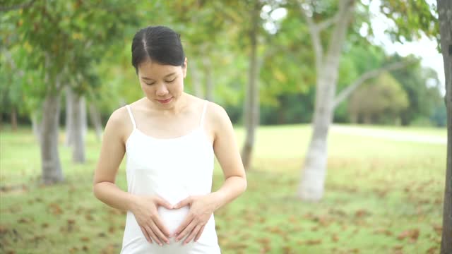 亚洲女性穿着孕妇装，双手抚摸着孕妇的新生命肚子视频素材