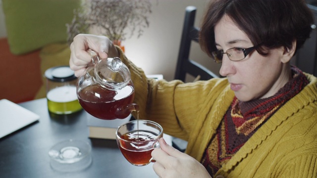 一个成熟的女人坐在桌子上倒一杯茶的特写视频素材