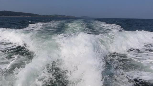 一艘摩托艇在安格尔西的梅奈海峡航行。海雀岛和海岸，蓝色的大海和夏天的天空。视频素材