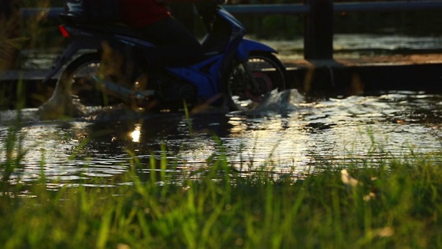 在大雨中，摩托车在被水淹没的城市街道上缓慢移动视频素材