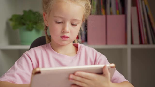 专注于小学女孩使用数字平板电脑学习和思考，她的手在家里的脸颊视频素材