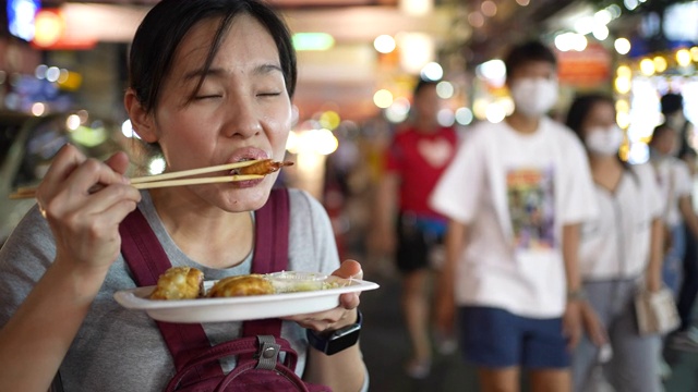 年轻的亚洲女人在街上吃街头小吃视频素材