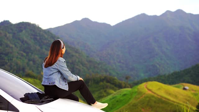 年轻女子坐在车上看美丽的山景，而驾驶公路旅行的假期视频素材