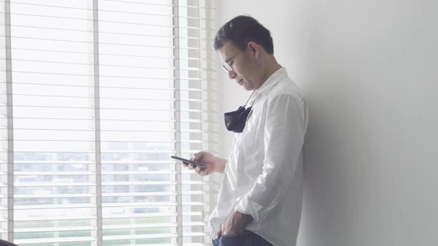 一个漫不经心的年轻男子戴着眼镜在俯瞰城市的窗户边打电话视频素材