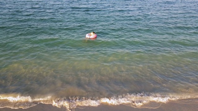 女人游泳和漂浮在海边的水与甜甜圈浮动鸟瞰图视频素材