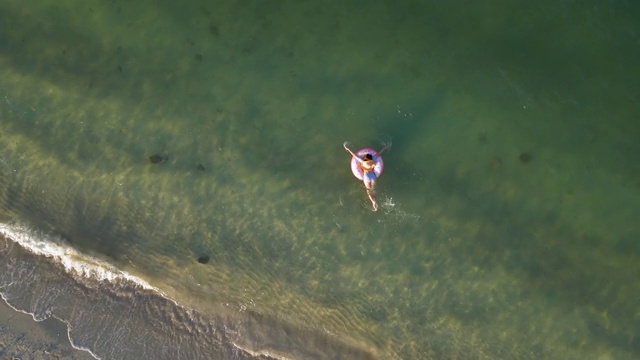 女人游泳和漂浮在海边的水与甜甜圈浮动鸟瞰图视频素材