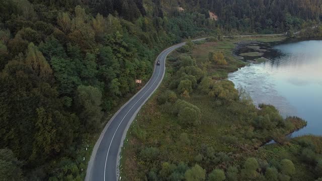 汽车通过森林和湖边的鸟瞰图。美丽的山路。在山路上开车。公路旅行。山地森林湖泊景观。汽车穿过松林视频素材