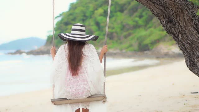 亚洲女人坐在吊床上绕着海、滩、海摇摆视频素材