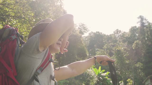 慢镜头低角度的疲惫的年轻亚洲男子背包客徒步旅行在美丽的森林山夏令营在夏天的一天。健康的帅哥在暑假放松享受户外生活方式视频素材