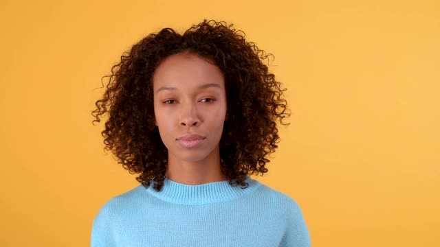 沉着自信的非洲裔美国妇女身穿蓝色毛衣的肖像。人在孤立的黄色背景。4 k视频素材