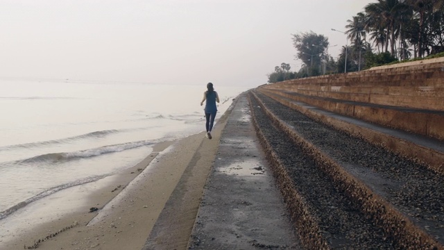 亚洲妇女在晨曦的背景下，在海边做热身运动和跑步。4 k慢动作。视频素材