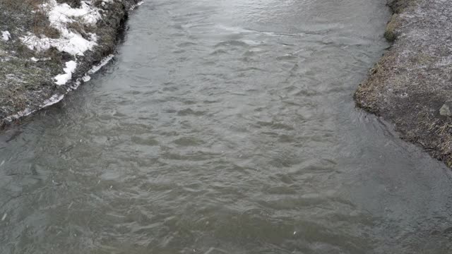 在一个阴沉的冬日，河上正在下雪。大片的雪花落在水面上。坏天气。冬天的风景。从上往下看。4 k。视频素材