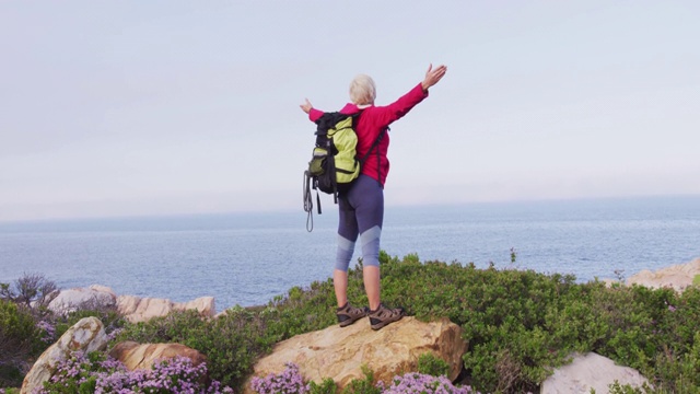 后视图的高级徒步女站着她的双臂张开站在岩石上，而徒步旅行视频素材