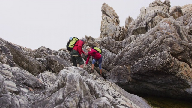 一对背着背包、拄着登山杖的资深徒步夫妇在攀岩时彼此牵着手视频素材