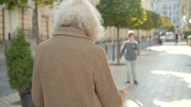 快乐的男孩沿着城市的街道跑向白发男子，拥抱着祖父。阳光明媚的日子里，快乐的白人孩子在户外会见祖父母。家庭的概念。视频素材