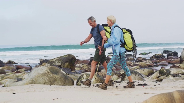 一对背着背包、拄着拐杖的老年徒步夫妇在徒步旅行时互相交谈和散步视频素材