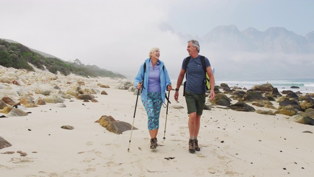 一对背着背包、拄着拐杖的老年徒步夫妇在徒步旅行时互相交谈和散步视频素材