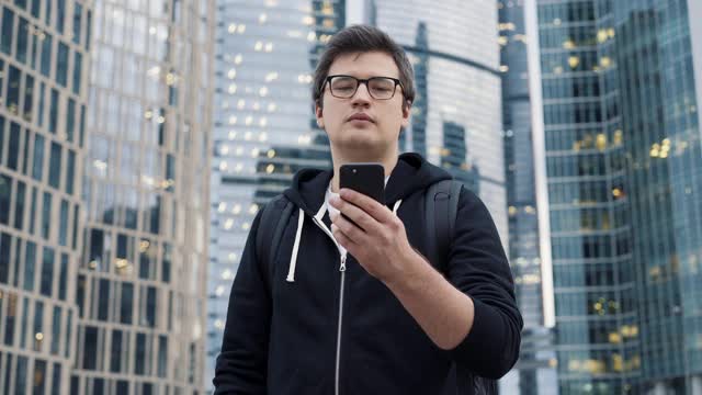 一名男子拿着手机站在商业中心摩天大楼的背景上视频素材