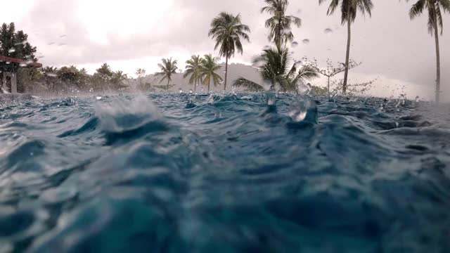 糟糕的假期的概念。大雨落进海边的豪华游泳池，背景是椰子树。视频素材