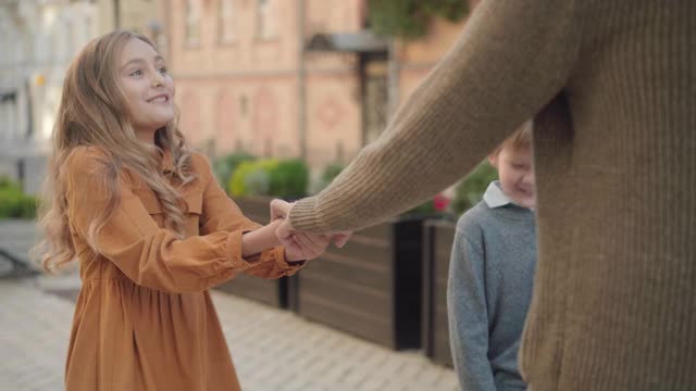 快乐的白人女孩和男孩在户外牵着老祖父的手。快乐的孙子和老人沿着城市的街道和有乐趣。视频素材