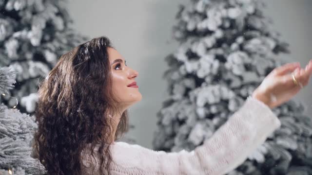 4k快乐女孩微笑，触碰新年除夕飘落的雪花。年轻女子靠近大雪杉在圣诞节前的冬天视频素材