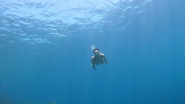 4K自由潜水长鳍海豚踢腿风格在大海的清澈的水后面的空气泡沫视频素材