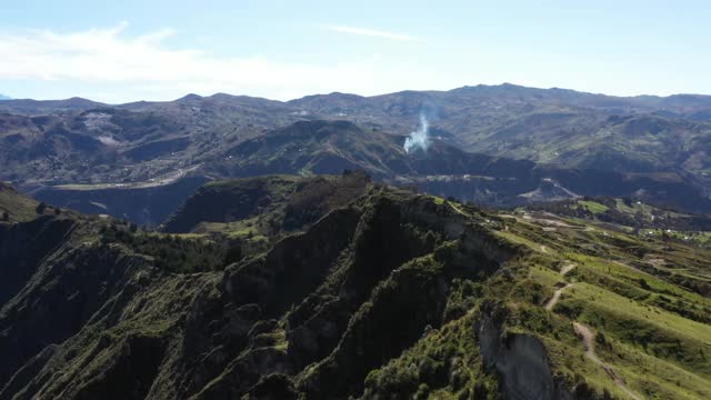 鸟瞰图飞过一个大山顶上的步道，背景是群山，可见一团大火的浓烟视频素材