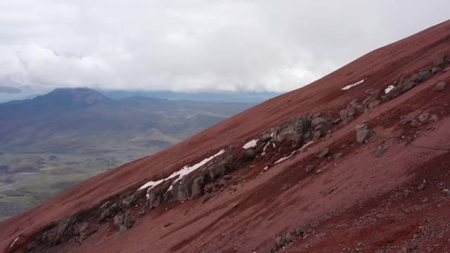 火山山坡覆盖着红色的沙子和一些大的岩石和一些从闪光的雪的残余视频素材