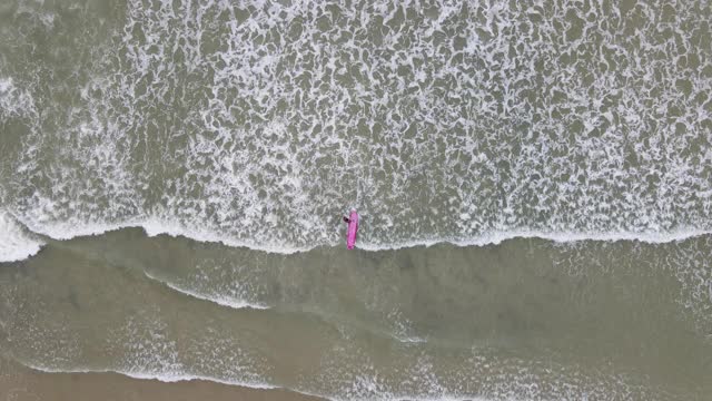 4k鸟瞰冲浪者带来他的冲浪板的大海视频素材