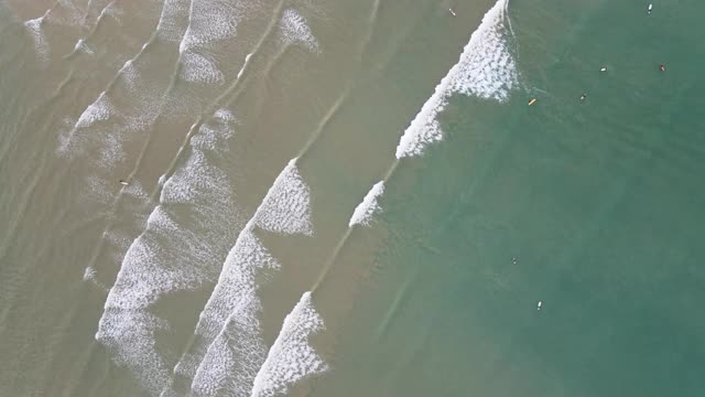 4k空中俯视图缩放在顺时针旋转的海滩波浪和冲浪者在海里视频素材