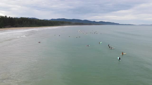 4k鸟瞰图通过多莉放大的海滩波浪和冲浪者在海里视频素材