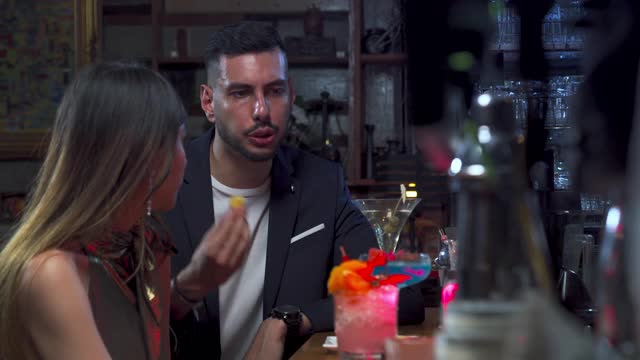 4K美丽的亚洲女人坐在吧台，与英俊的男人聊天，在夜店派对上喝着美味的鸡尾酒。男酒保为顾客准备混合酒精饮料。视频下载