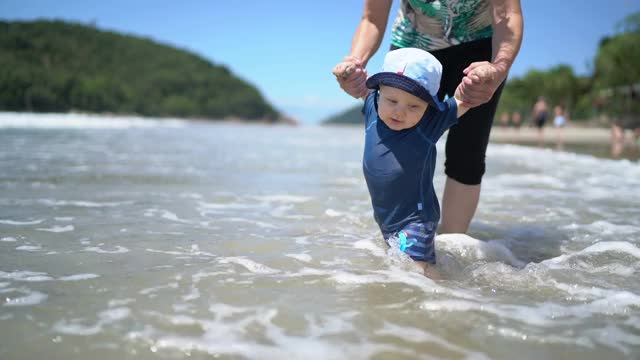 第一次在海滩上被牵着手进入大海的小男孩视频素材