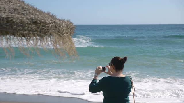 一个女人在西班牙的海岸拍照，4k慢镜头60fps视频素材