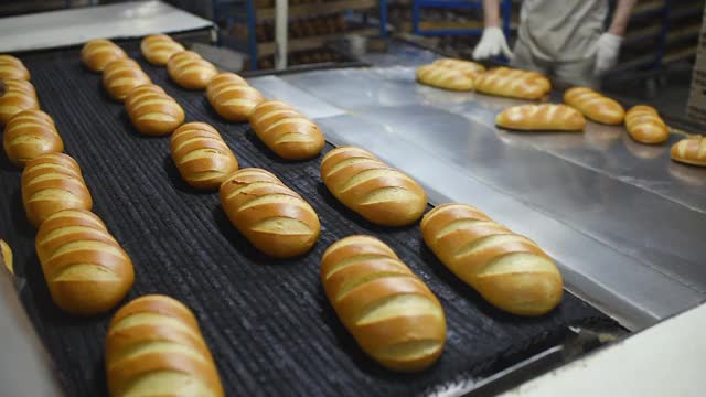 年轻的男面包师在生产线或面包容器的背景下从烤箱中取出新鲜芳香的热面包和糕点。视频素材