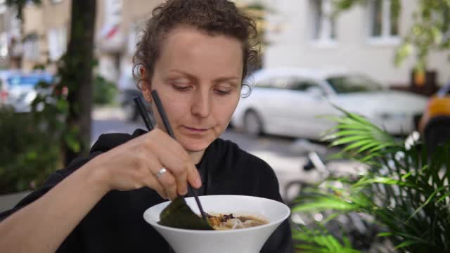 侧面的饥饿妇女吃蔬菜丰富的味增面与筷子在公园。健康的素食亚洲街头小吃视频素材