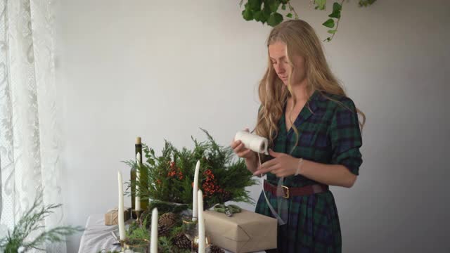 节日、新年和圣诞节概念——一个女人站在节日的桌子旁，用一个盒子装一份礼物视频素材