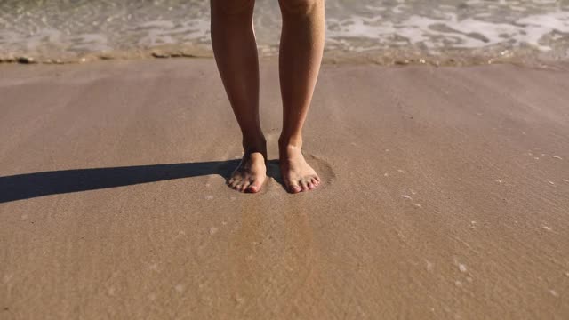 脚被海浪冲掉了。海浪滚在沙滩上洗女人的脚站在潮湿的边缘下阳光近距离。在海上休息视频素材