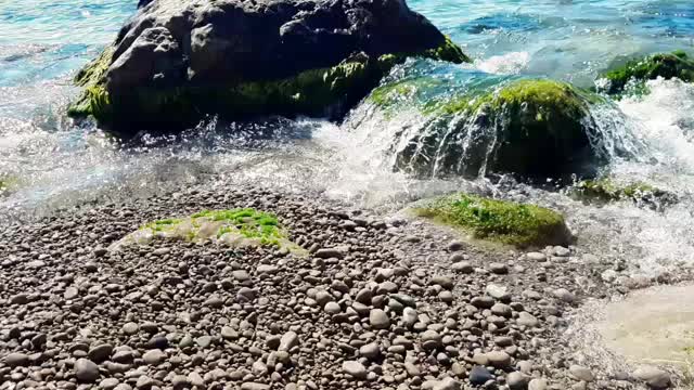 大海里清澈的水在小波浪中流淌在卵石滩的岩石岸边，水中有巨大的卵石。视频素材