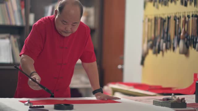 亚洲华人男性练习书法，为即将到来的中国新年庆祝家庭装饰目的与繁荣和良好的措辞写在一张红色的纸上视频素材